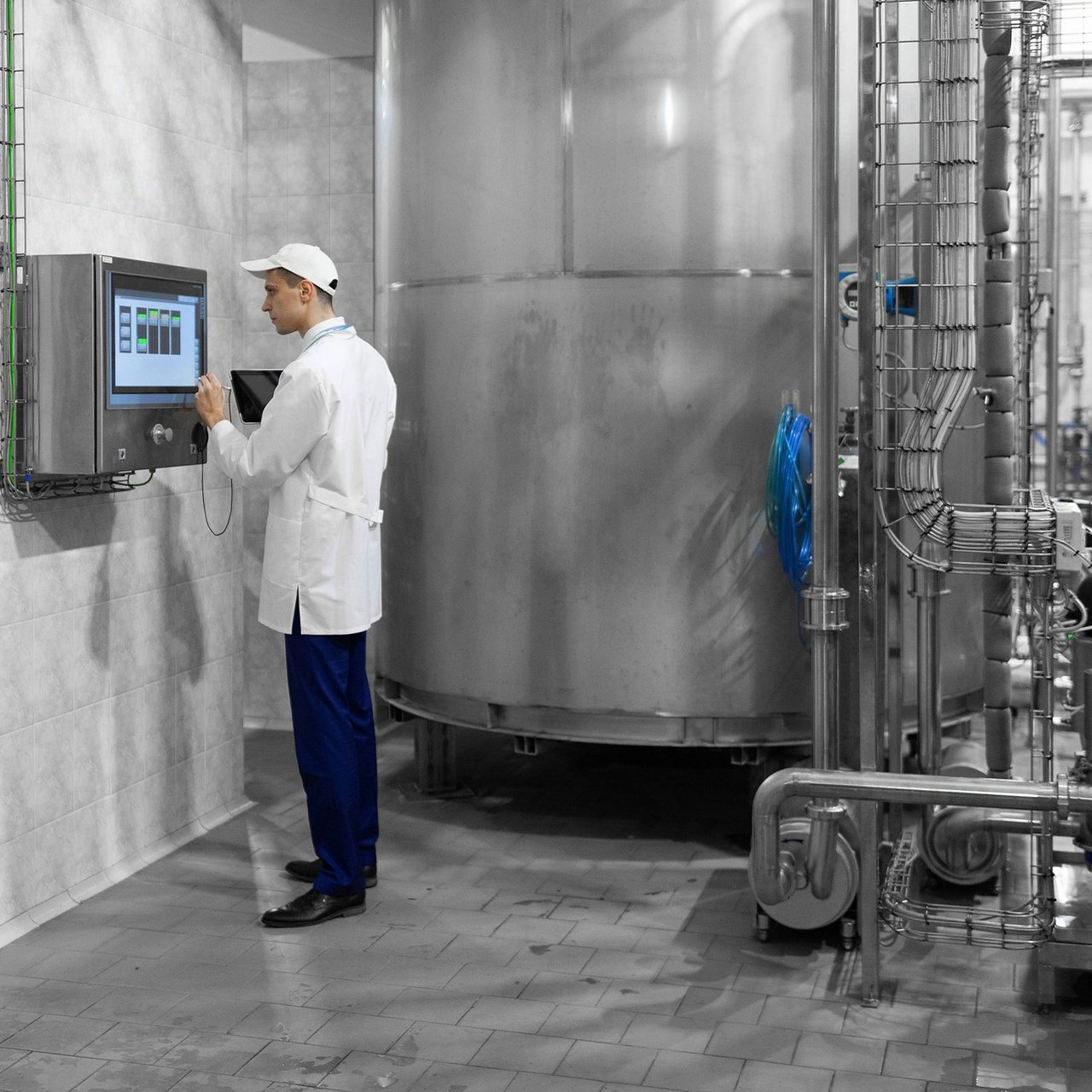 Mitarbeiter im weißen Kittel bedient ein Touchscreen vor einer großen Edelstahlanlage in einer Industriehalle.