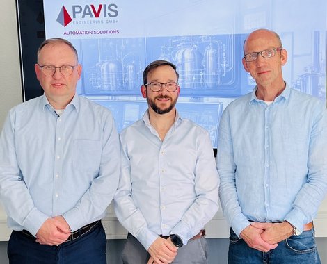 Drei Männer in hellblauen Hemden posieren vor einem Monitor mit dem PAVIS-Logo – Automation Solutions.